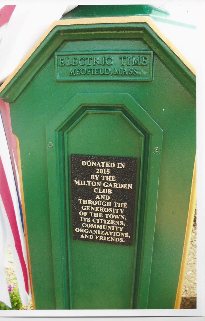 This photo shows a closeup of the dedication plaque on the green clock tower, from "Electric Time, Medfield, Mass". The plaque says "Dedicated in 2015 by the Milton Garden Club and through the generosity of the town, its citizens, community organizations, and friends."