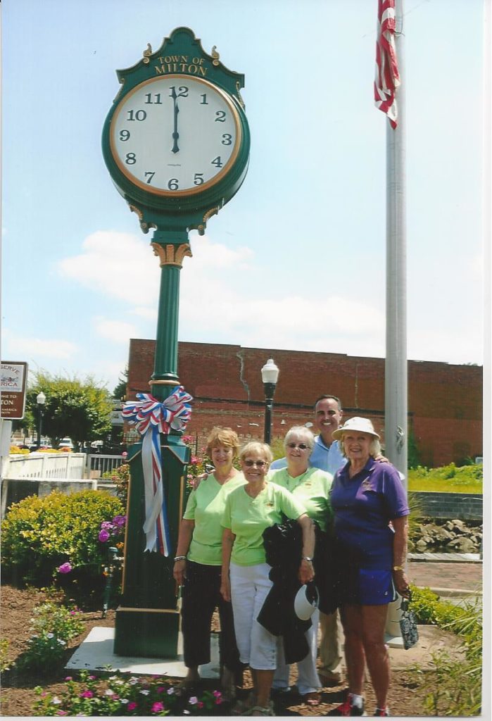 Photo showing Milton Garden Club members standing below US Flag and green clock tower at noon on July 26, 2015.